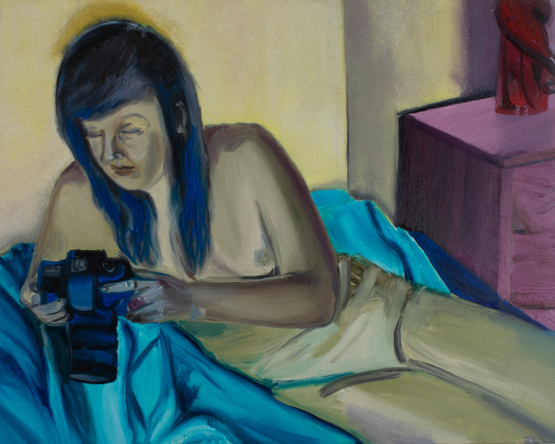 Olive green femme nude figure repose on blue bed gazing upon a hand held camera.